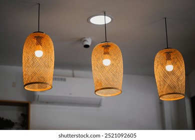 Three elegant woven pendant lights suspended from the ceiling, casting a warm glow in a modern interior setting, creating a cozy and inviting atmosphere. - Powered by Shutterstock