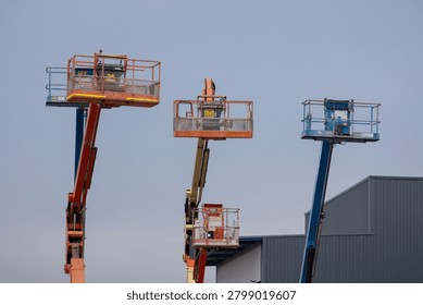 Three elevated work platforms raised against a clear sky. Each platform has safety rails and lifting arms. One unit extends highest, another is mid-height, third lowest