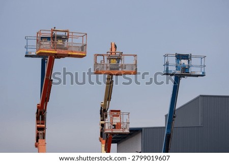 Three elevated work platforms raised against a clear sky. Each platform has safety rails and lifting arms. One unit extends highest, another is mid-height, third lowest
