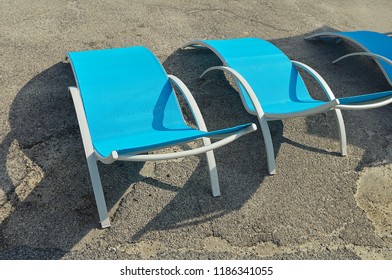 Three empty beach chairs made of metal and plastic on the asphalt pavilion