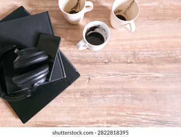 Three empty coffee cups beside a closed laptop, notebook and headphones on a wooden desk with copy space. Concept of finished workday, productivity and burnout.
