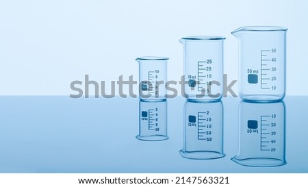 Three empty measuring beakers sitting on a mirror blue surface, glass lab containers standing in gradual order on a table, transparent light through laboratory flasks, precise comparing measurements 