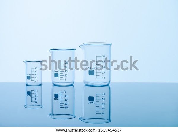 Three empty measuring beakers sitting on a mirror blue\
surface, glass lab containers standing in gradual order on a table,\
transparent light through laboratory flasks, precise comparing\
measurements 