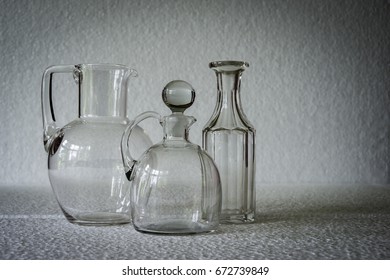 Three empty old fashioned clear glass flasks, one bottle-shaped and one with with glass stopper, all casting a slight shadow against a dappled white background with space on which to overprint text