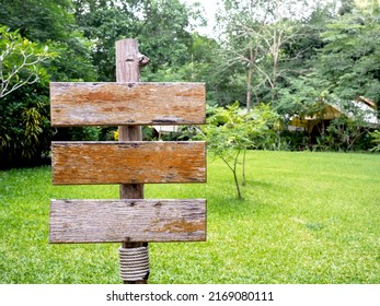Three empty old wood plank signs on the wooden pole near the green grass garden with copy space. Collection of various wooden sign on the yard.
