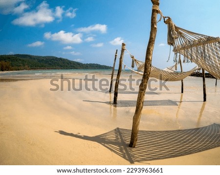 Three empty rope cradle hanging on the wooden poles on sandy beach, island and blue sky background, fisheye view. Beautiful shadow of hanging cradle or swing beds on clean sand beach.