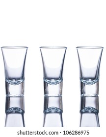 Three Empty Shot Glasses On A Reflective Surface. Isolated On White.