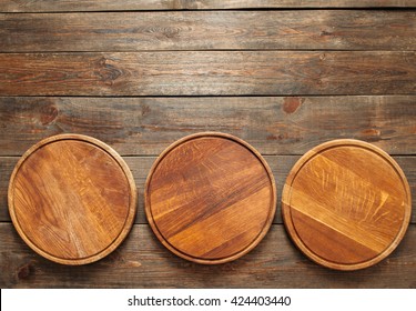 Three empty wooden pizza plates lie on the wooden table at the bottom of the picture. Copy space. Horizontal line. Flat lay of empty wooden pizza plates