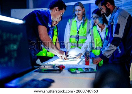 Three engineers leaning over blueprints on an illuminated planning table aligning on the pour sequence, a radio and hard hat within reach in the dark planning room late in the day.