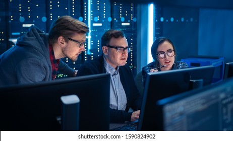 Three IT Engineers / Programmers Talking about Work, Using Computers. Technical Department with Data Server Racks. Software Development / Code Writing / Website Design / Database Architecture - Powered by Shutterstock