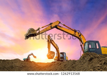 Three excavators work on construction site at sunset