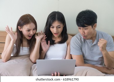 Three Excited Friends Or Roommates Watching Tv On Line In Laptop Sitting On Bed.