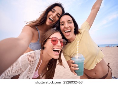 Three excited young Caucasian friends in summer clothes taking selfie on beach. Group of smiling women enjoying vacation. Cheerful beautiful girls of generation z pose for photo with mobile phone. - Powered by Shutterstock