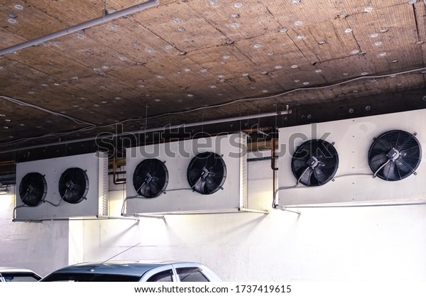 Three external heat exchange\
units of the air conditioning system on the wall of the open\
Parking floor under the modern building. Thermal insulation on the\
ceiling.