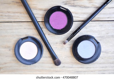 Three Eyeshadow Boxes And Brushes On Wood Table