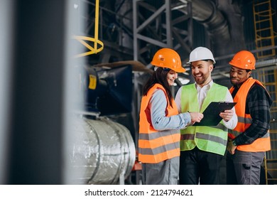 Three factory workers in safety hats discussing manufacture plan
