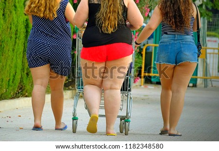 three fat girls are taking food in a basket from a supermarket down the street. view from the back	
