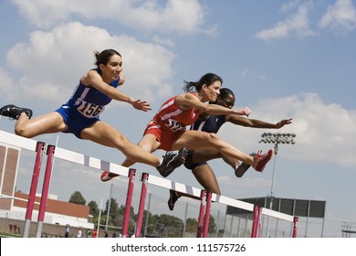 Three female athletes clearing hurdles in race - Powered by Shutterstock