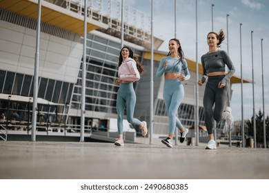 Three female athletes running in urban setting, exuding health, vitality, and camaraderie. - Powered by Shutterstock