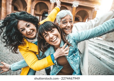 Three female best friends having fun together walking on city street - Happy mature women smiling at camera outside - Friendship concept with aged people hanging out on a sunny day - Backlight filter - Powered by Shutterstock