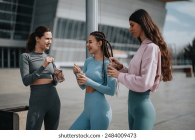 Three female friends chatting and eating healthy smoothie post-exercise in urban setting - Powered by Shutterstock