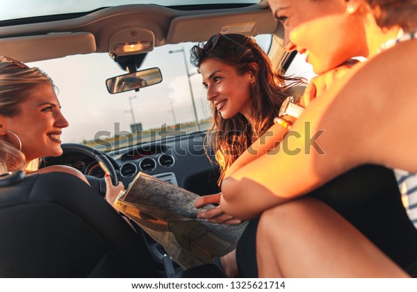 Three female friends enjoying traveling at vacation\
in the car.