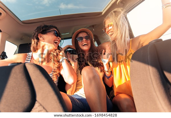 Three female friends\
enjoying traveling in the car. Sitting in rear seat and having fun\
on a road trip.