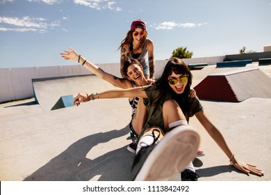 Three female friends playing with skateboard at the skate park. One woman pushing her friends from behind having fun and laughing. - Powered by Shutterstock