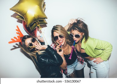 Three female friends posing in front of white wall. New year party