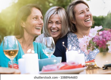 drei Freundinnen in ihren 40ern teilen einen Moment der Mittäterschaft. Sie versammelten sich um einen Tisch im Garten, um ein Essen mit Freunden zu teilen.
