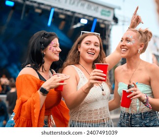 Three Female Friends Wearing Glitter Having Fun At Summer Music Festival Holding Drinks - Powered by Shutterstock