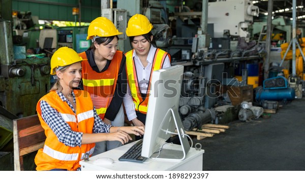 Three female mechanical engineers or factory\
workers in safety uniform work with computer to check the factory\
operation in a warehouse