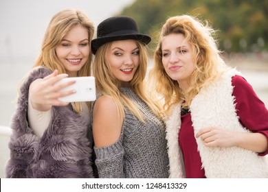 Three females taking selfies, having fun outdoor using smart phone to take photo.