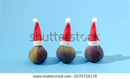 Three figs with Santa's red caps with white pompoms on pastel blue background. Funny and surreal Christmas or New Year creative concept.