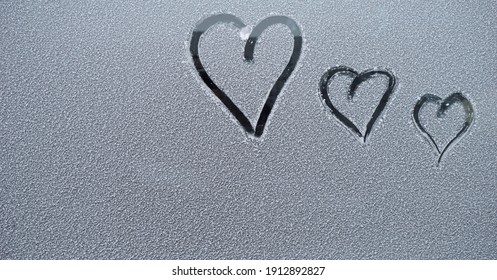   three finger-drawn hearts on snow-covered glass                             