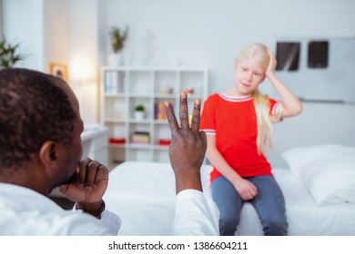 Three Fingers. Dark-skinned Doctor Wearing Uniform Showing Girl With Concussion Three Fingers