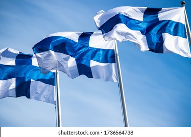 Three finnish national flags on the wind against the blue sky