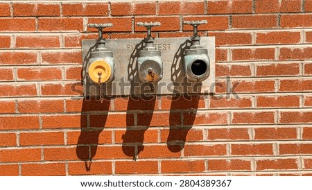 Three fire hydrants mounted on a brick wall show connections for testing. One hydrant has a yellow cap, while the other two are grey and black.