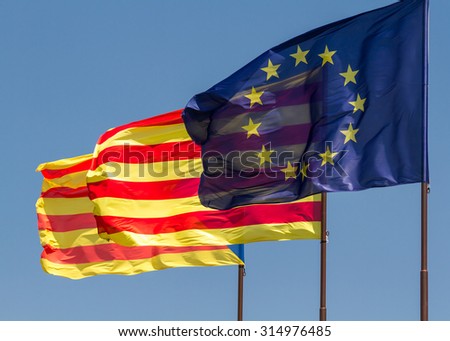 Three flags fluttering together on a windy day: the flag of the European Union and the ancient flag of Catalonia.