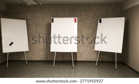 three flip chart boards set up in empty classroom with stone wall background. boards secured with clips, clean and organized space, educational environment, flipchart ready for lesson or meeting