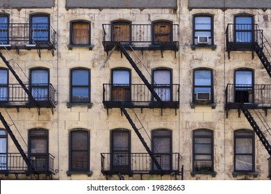 Three floors of windows with fire escapes on the facade of a New York apartment building that is in desperate need of paint and repairs.
