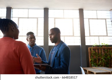 Three Focused Young African Business Colleagues Deep In Conversation Together While Standing In A Large Modern Office