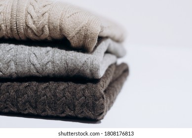 Three folded cashmere knitted sweaters in different shades of gray on white background. three shades of gray. Stack of three sweaters isolated on black background. Knitted wool sweaters.
