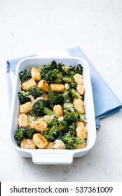 Three Fourth Angle Of Rich Green Broccoli And Baked Tater Tots Casserole Topped With Grated Parmesan Cheese And Black Pepper On Light Blue Linen In Simple White Casserole Dish On Cream Marble Surface.