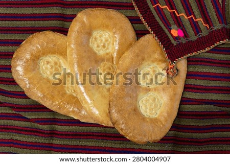 Three fresh baked Turkmen flatbreads known as chorek with traditional stamped patterns. The golden crust breads are arranged on a striped woven textile backdrop.