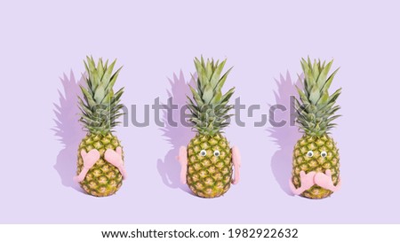 Three fresh pineapples like three wise monkeys. Concept of see no evil, hear no evil and speak no evil. Summer fruit on pastel purple background.