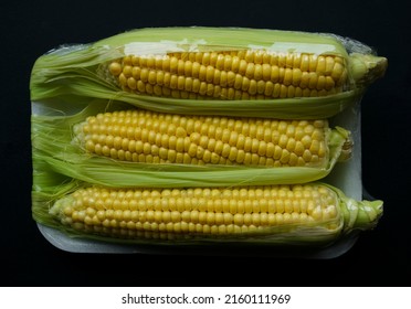 Three fresh ripe yellow corn on cobs. Packed in plastic foil. vacuum packed fresh corn isolated on black  background. - Shutterstock ID 2160111969