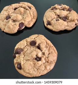 Three Freshly Baked Cookies Sitting On A Black Cookie Sheet. Organic Chocolate Chip Cookies. Soft, Warm And Gooey Chocolate Chip Cookies Fresh Out Of The Oven.