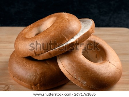 Three freshly baked plain bagels piled on a rustic wooden cutting board, ready for breakfast or as a bakery display