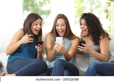 Three Friends Amazed Watching A Smart Phone Sitting On A Couch At Home